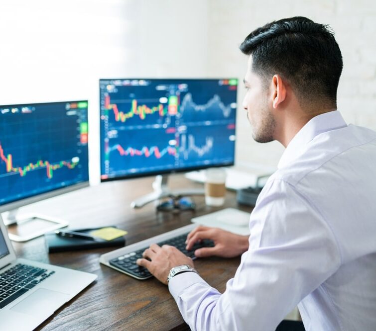 Inversor analizando gráficos financieros y operando en plataformas de trading en varias pantallas